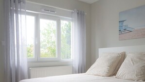 Makuuhuoneessa on suuri sänky, ikkunassa verhot, patteri ja seinällä taulu.