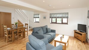 A spacious living area with a sofa, coffee table, TV stand, and dining set. - Bwthyn Cae Haidd (Beaumaris)