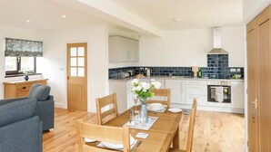 A modern kitchen with white cabinets, a black tiled backsplash, and a wooden dining table set for four. - Bwthyn Cae Haidd (Beaumaris)