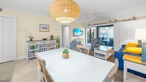 Ein geräumiger Wohnbereich mit einem großen Esstisch, einer bequemen Couch und einem Deckenventilator.