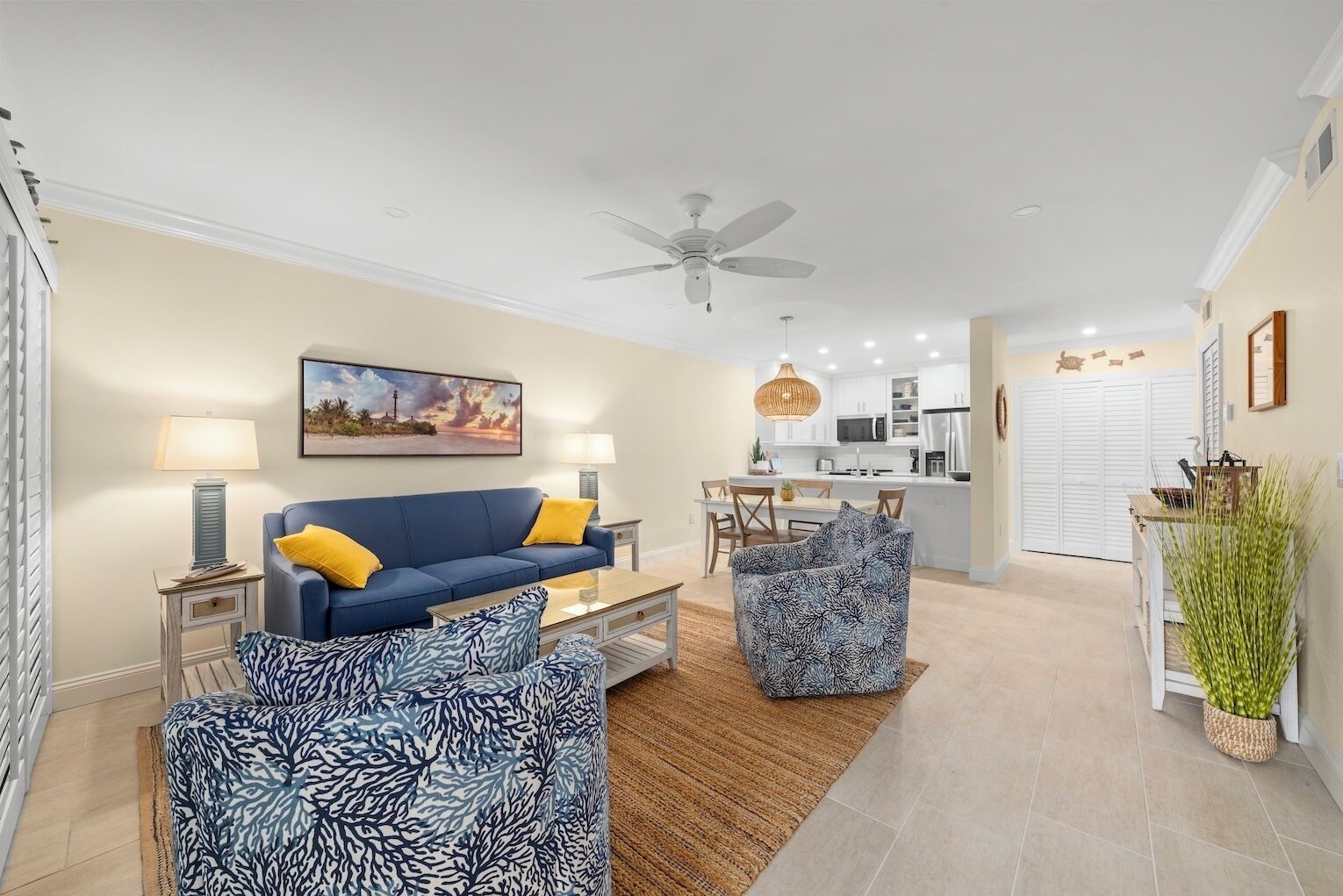 A modern living room with a blue sofa, patterned ottoman, and a dining area with a table and chairs.