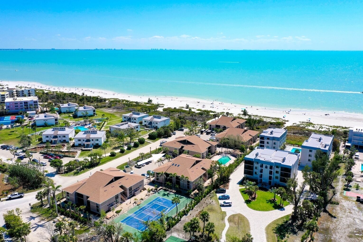 An aerial view of a coastal resort with multiple buildings, a beach, and a clear blue sea.