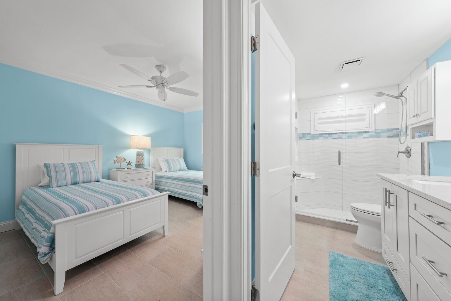 A bedroom with two beds, a ceiling fan, and a bathroom with a shower, toilet, and sink.