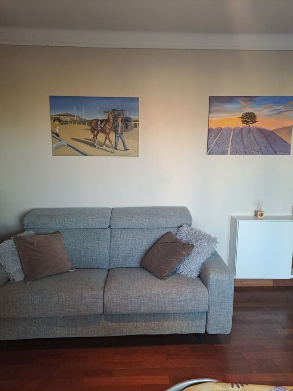 A living room with a grey sofa, two brown cushions, a white sideboard, and two paintings on the wall.