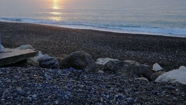 Une plage de galets avec un coucher de soleil sur l’océan.