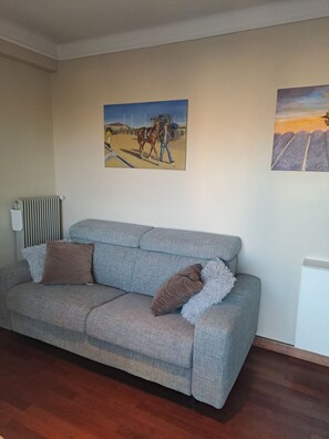 Ein Wohnzimmer mit einem grauen Sofa, zwei braunen Kissen und zwei Bildern an der Wand.