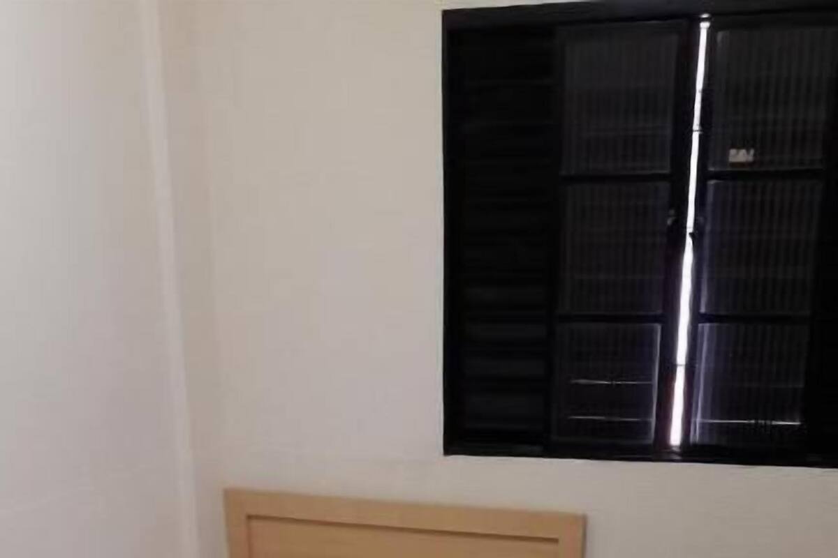 Una cama individual con cabecera de madera, una mesita de noche y una ventana con persianas cerradas.