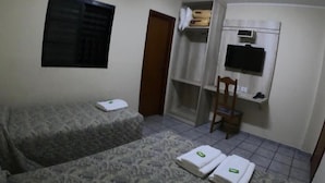 Una habitación pequeña y sencilla con una cama, una silla, un televisor y un estante con objetos.