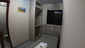 Una habitación pequeña y funcional con cama, armario, inodoro y ventana con persiana negra.