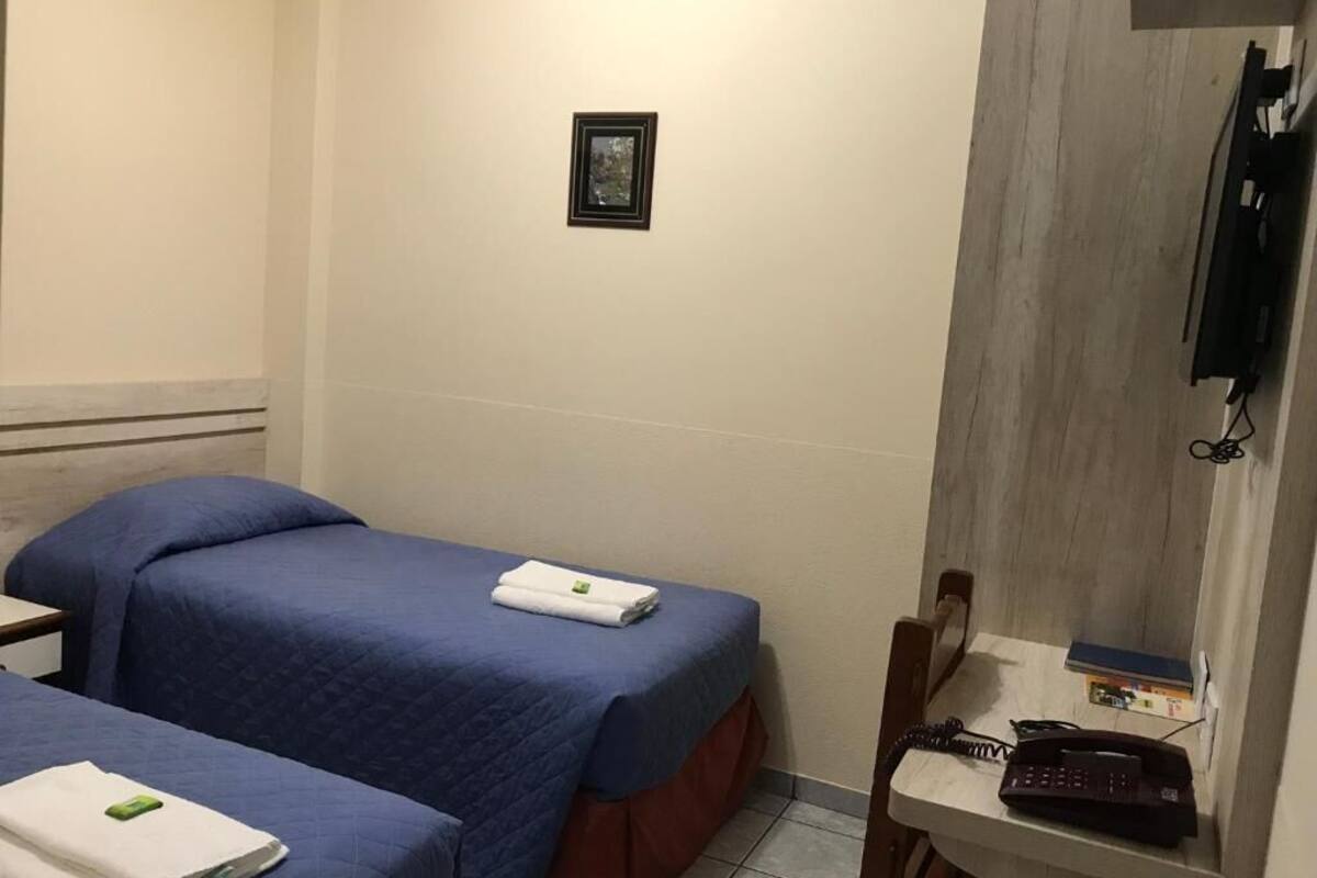Una habitación de hotel con dos camas, un escritorio pequeño, un teléfono y un cuadro en la pared.