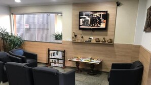 Zona de recepción con sillas negras, un televisor en la pared, una estantería y una pequeña mesa con revistas.