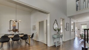 A spacious dining area with a wooden table and chairs, a hanging light fixture, and a view of the upper floor. - Spacious & Cozy Texas Gem with Private Pool (Plano)