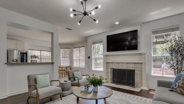 A spacious living room with a fireplace, a television mounted on the wall, and a dining area with a table and chairs. - Spacious & Cozy Texas Gem with Private Pool (Plano)