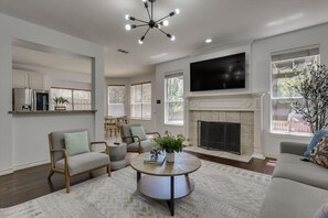 A spacious living room with a fireplace, a television mounted on the wall, and a dining area with a table and chairs. - Spacious & Cozy Texas Gem with Private Pool (Plano)
