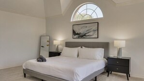 A bedroom with a bed, two bedside tables, a large window, and a painting on the wall. - Spacious & Cozy Texas Gem with Private Pool (Plano)