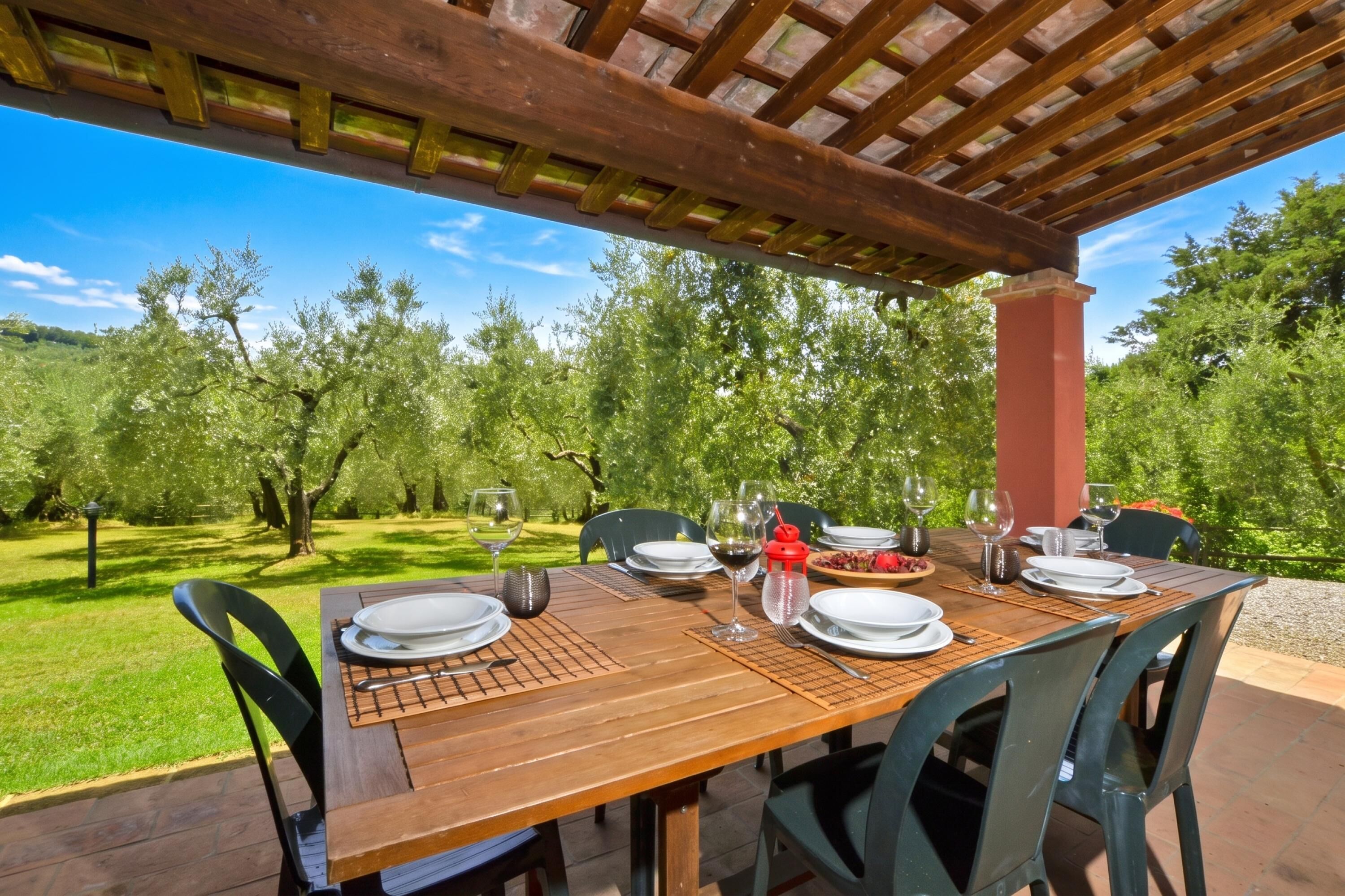 An outdoor dining area with a wooden table set for four, surrounded by chairs, under a wooden pergola.