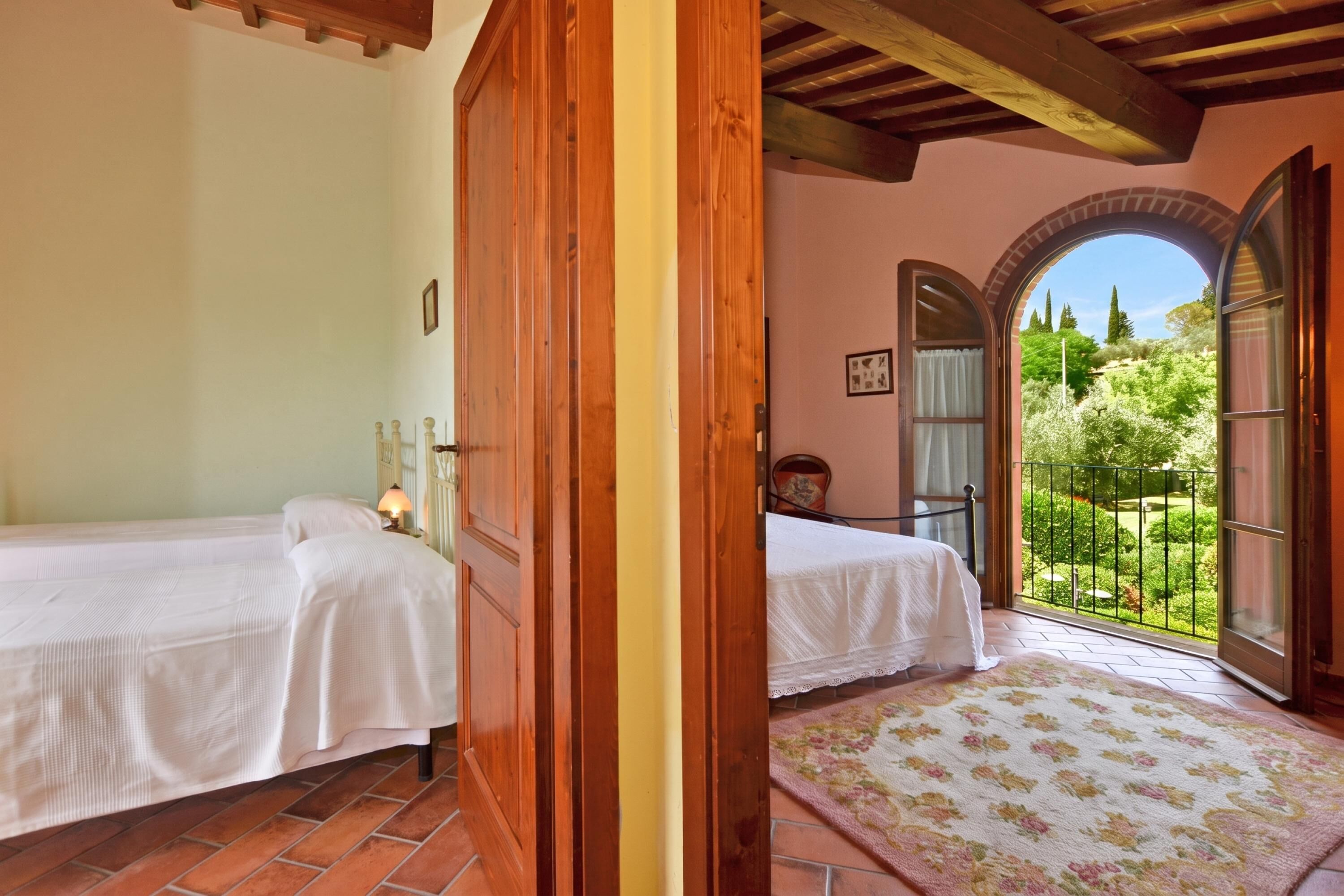 A bedroom with two beds, a wooden door, and a view of a garden through an open door.