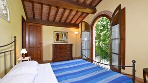 A bedroom with a bed, wooden dresser, and a view through an arched window.