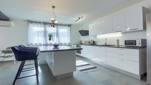 A modern kitchen with a central island, white cabinetry, a built-in microwave, and a dining area with a blue chair. - Villa Ancora - holiday house near the sea with a pool for up to ten guests by MyWaycation (Seget Donji)