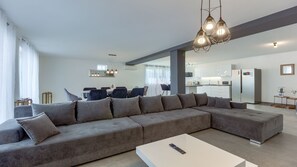 A modern living room with a large grey sectional sofa, a white coffee table, and a dining area in the background.