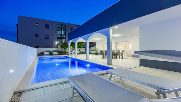 A modern outdoor pool area with lounge chairs, a covered seating area, and a building in the background. - Villa Ancora - holiday house near the sea with a pool for up to ten guests by MyWaycation (Seget Donji)