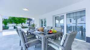 A dining area with wicker furniture, a table set with plates, glasses, and a fruit bowl. - Villa Ancora - holiday house near the sea with a pool for up to ten guests by MyWaycation (Seget Donji)