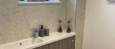Ein modernes Badezimmer mit Marmorwaschbecken, Holzschränken, einer Toilette und einem Fenster mit Topfpflanzen.