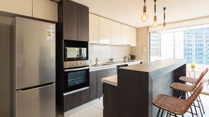 A modern kitchen with a built-in oven, a refrigerator, and a bar area with wicker chairs. - Arauco Wood - 2BR, Parking, Wifi, Mall & Pool (Vitacura)