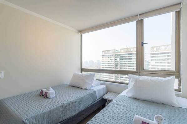 Una habitación de hotel con dos camas, un ventanal con vistas a la ciudad y una mesita.