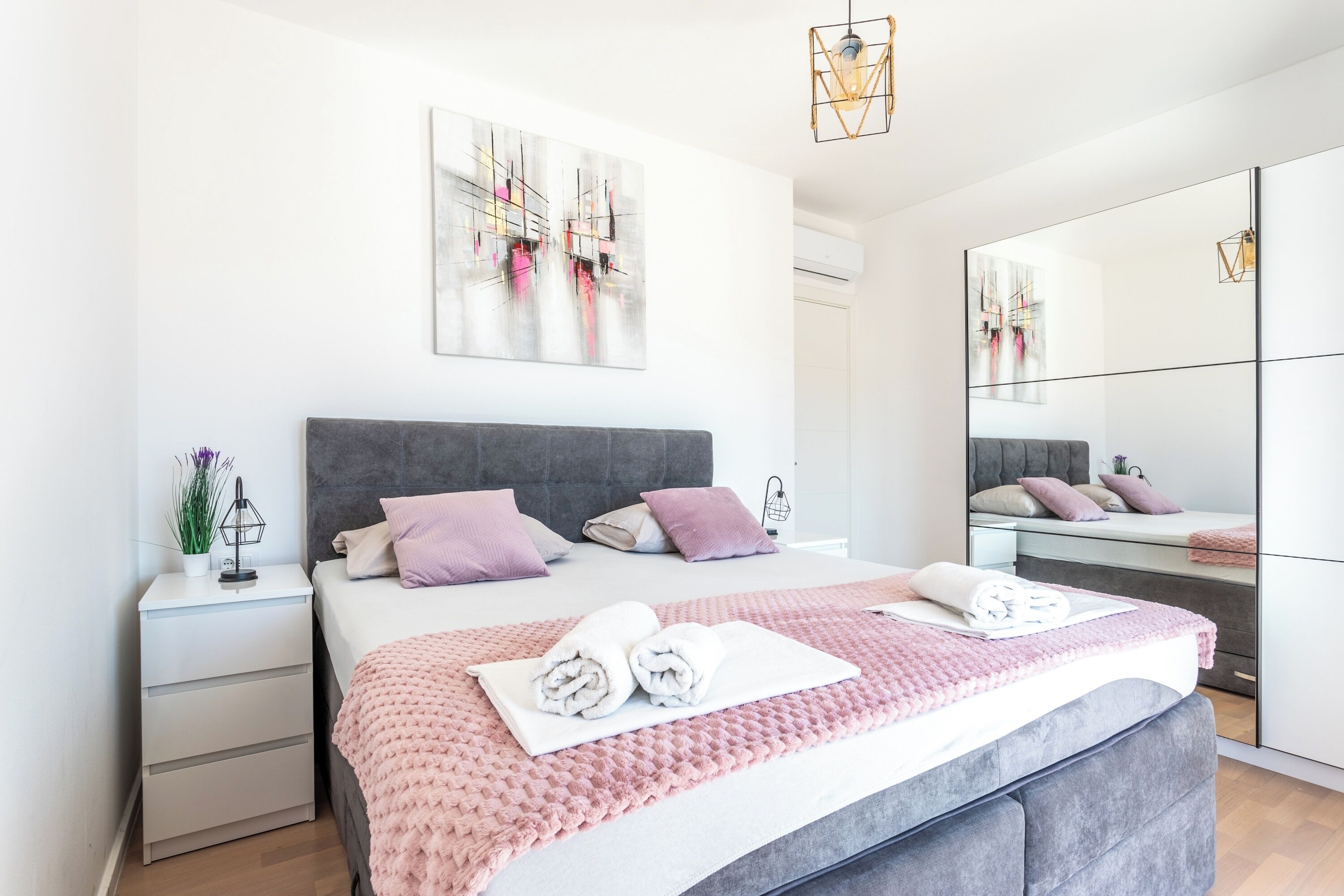 Une chambre moderne avec un grand lit, une table de chevet, un miroir et des œuvres d’art abstraites accrochées au mur.