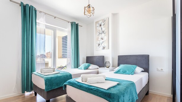 A hotel room with two beds, teal curtains, a city view, and a modern light fixture. - Luxury Modern Penthouse w Jacuzzi & Huge Terrace (Split)