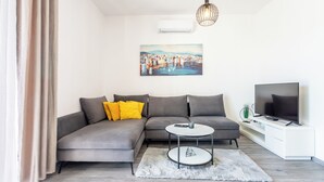 A modern living room with a grey sofa, a round coffee table, a flat-screen TV, and a painting on the wall. - Luxury Modern Penthouse w Jacuzzi & Huge Terrace (Split)