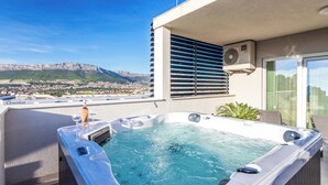 A hot tub on a balcony with a city view, a window with blinds, and an air conditioning unit. - Luxury Modern Penthouse w Jacuzzi & Huge Terrace (Split)