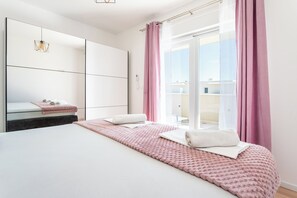 A modern bedroom with a large bed, a bedside table, a mirror, and a view of the outdoors through a sliding glass door. - Luxury Modern Penthouse w Jacuzzi & Huge Terrace (Split)