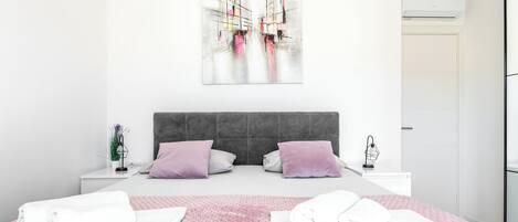 A modern bedroom with a large bed, two nightstands, a gray headboard, and a wall-mounted air conditioner.