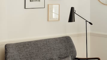 Ein modernes Wohnzimmer mit einem gemusterten Sofa, einer Stehlampe und gerahmten Bildern an der Wand.
