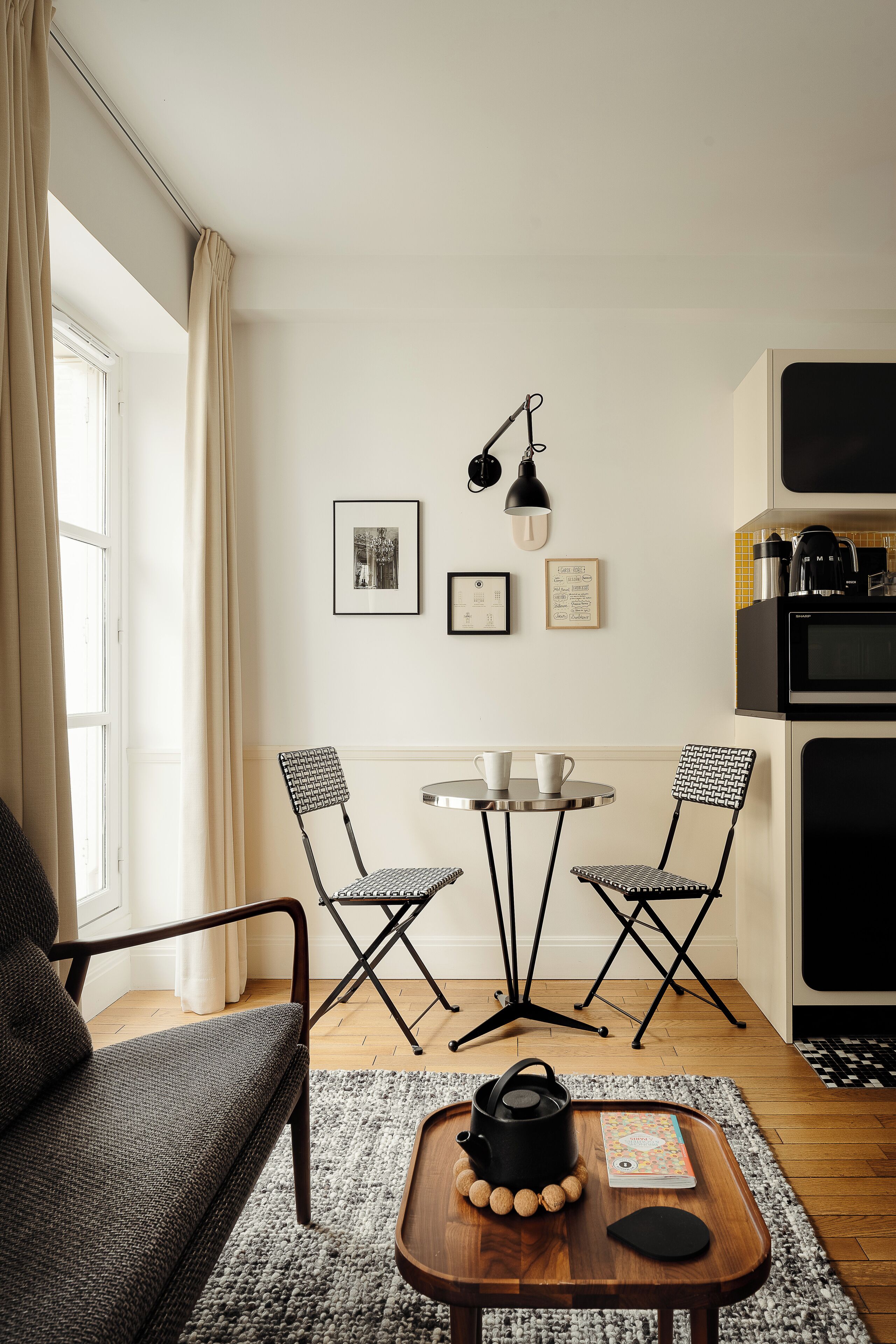 A modern kitchen with a dining area, featuring a sofa, two chairs, a small table with a kettle, and a coffee machine.