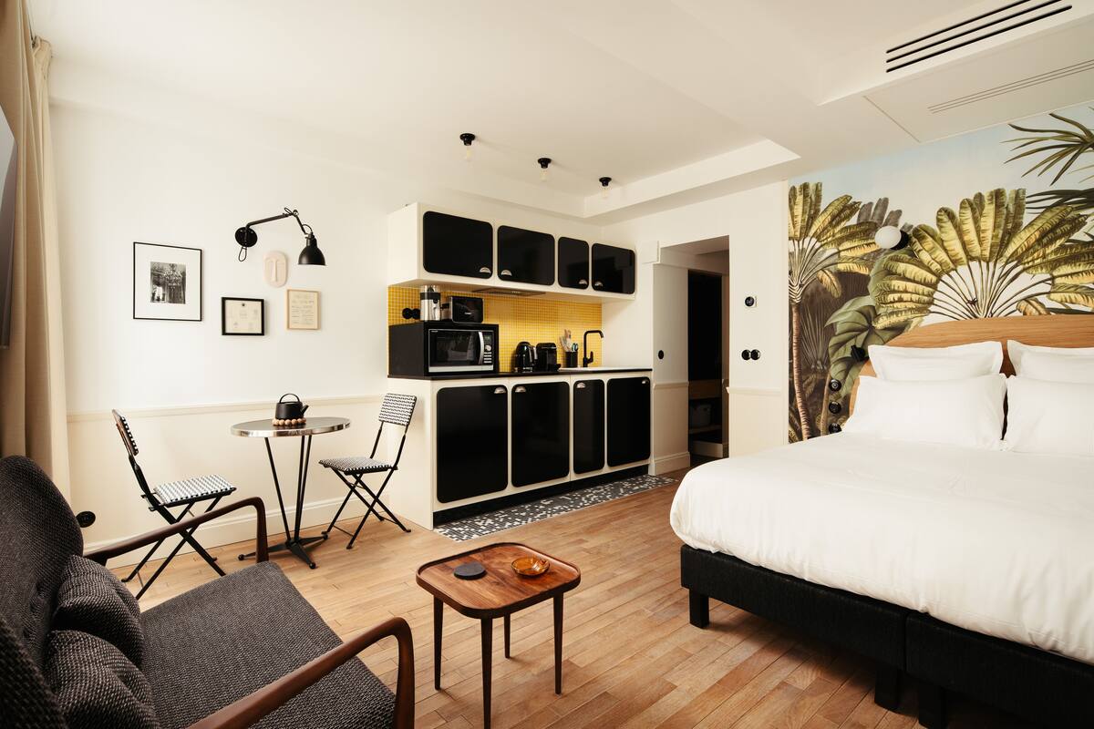 Ein Hotelzimmer mit einem Bett, einem kleinen Tisch, einem Sessel, einer Küchenzeile und einem Essbereich.
