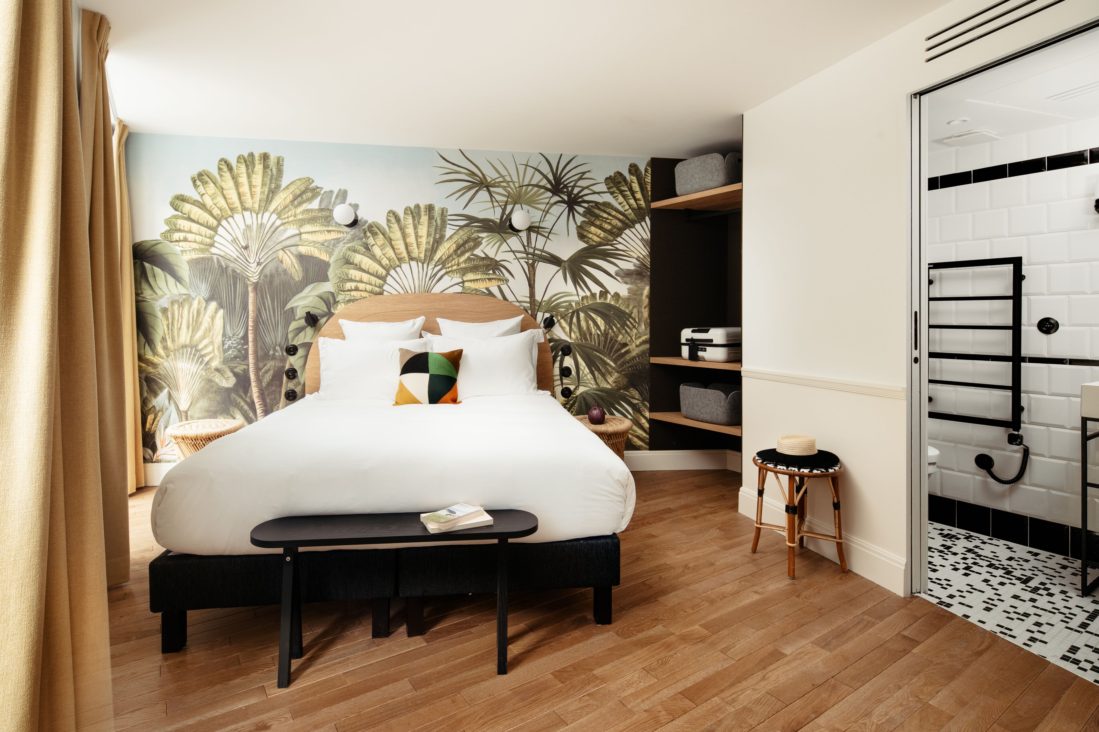 Une chambre à coucher avec un grand lit, une petite table, un banc, une armoire et une salle de bain dont un mur est recouvert de carreaux.