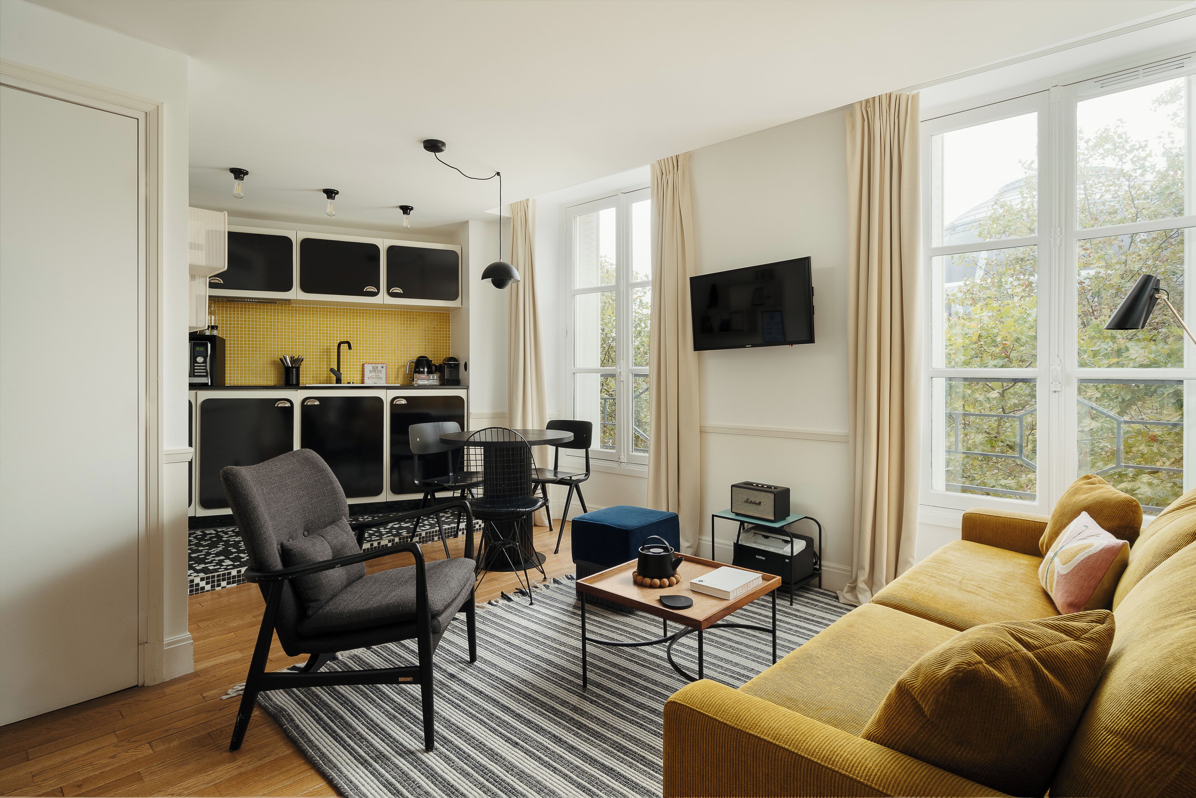 A compact living space with a kitchenette, a sofa, a dining area, and a TV mounted on the wall.