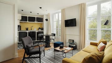 A compact living space with a kitchenette, a sofa, a dining area, and a TV mounted on the wall.