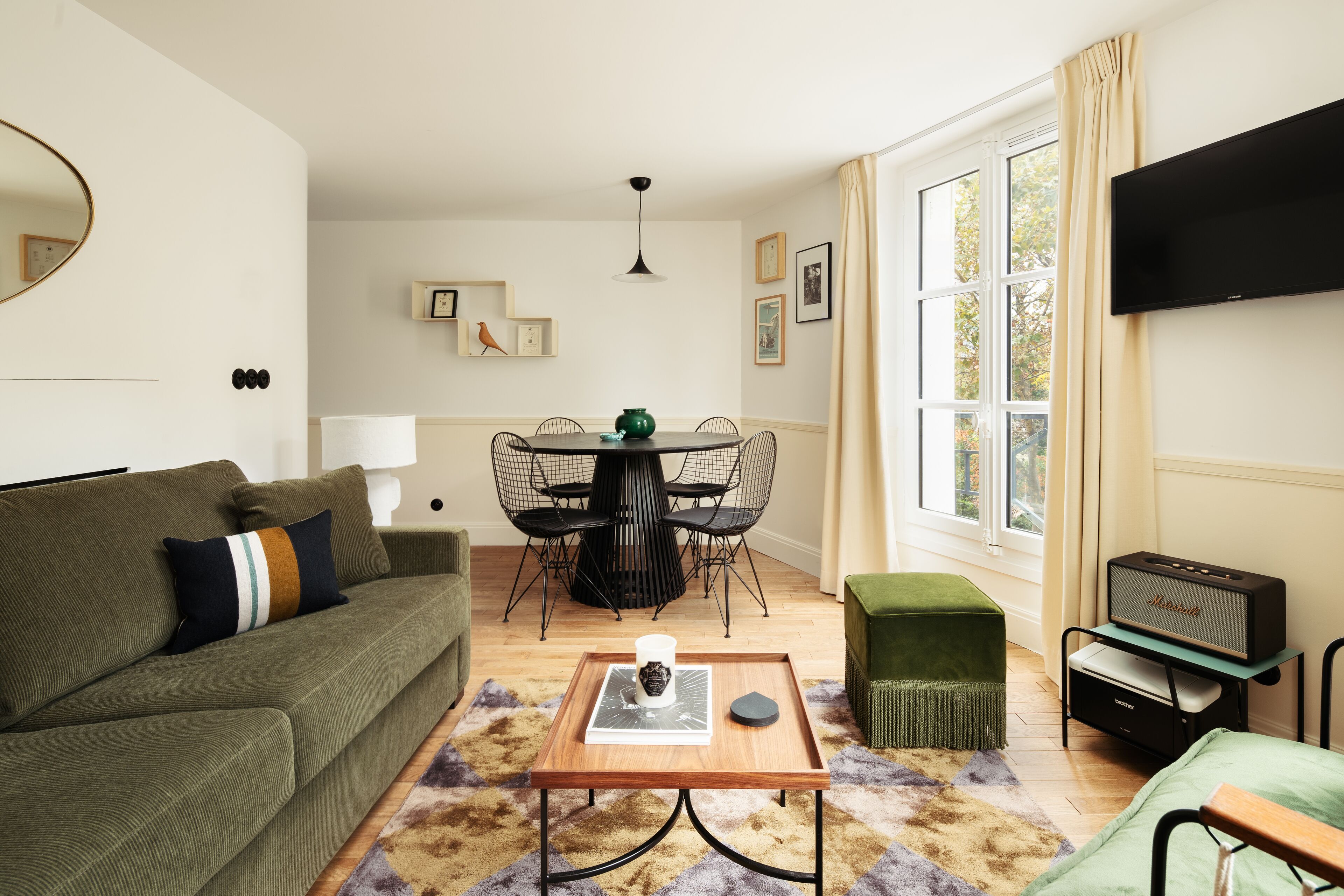 A living room with a green sofa, a coffee table, a TV, and a dining area with a table and chairs.