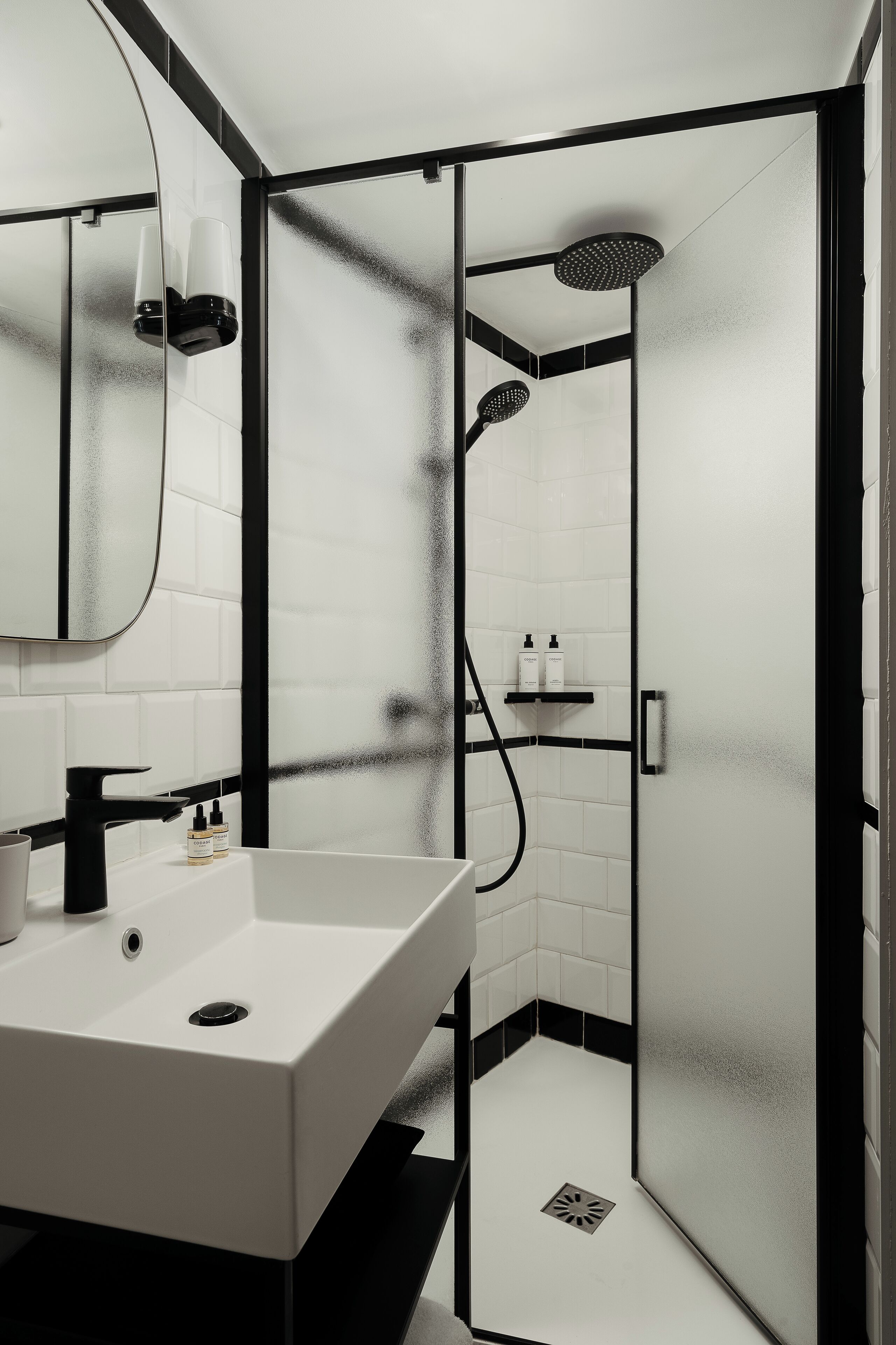A modern bathroom with a white sink, black faucet, and a glass shower enclosure.