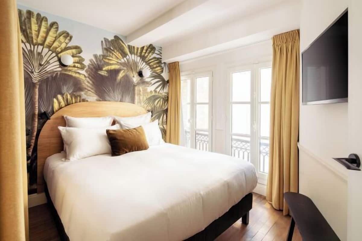 Ein Hotelzimmer mit einem großen Bett, einem an der Wand befestigten Fernseher und einem Balkon mit Vorhängen.