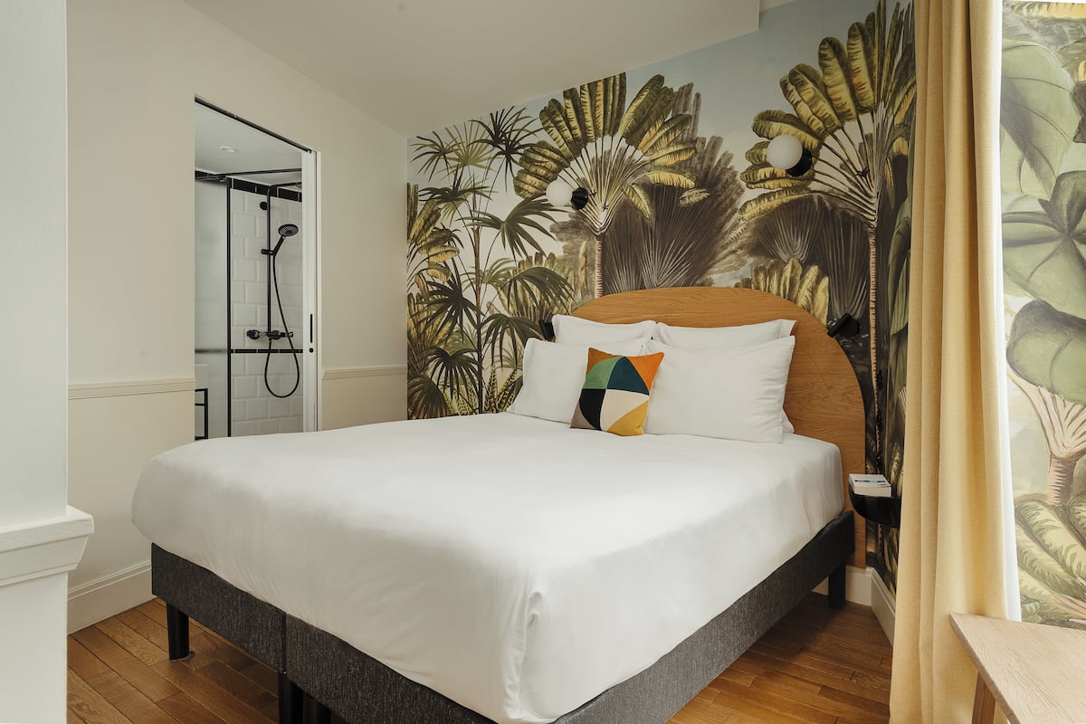 Ein Hotelzimmer mit einem großen Bett, einer Dusche und einem Wandbild mit tropischen Pflanzen.