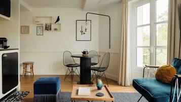 A modern living room with a blue sofa, a wooden coffee table, and a dining area with a round table and chairs.
