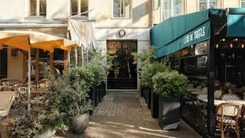 En udendørs café med borde, stole og plantekasser, samt en bygning indgang med et skilt.