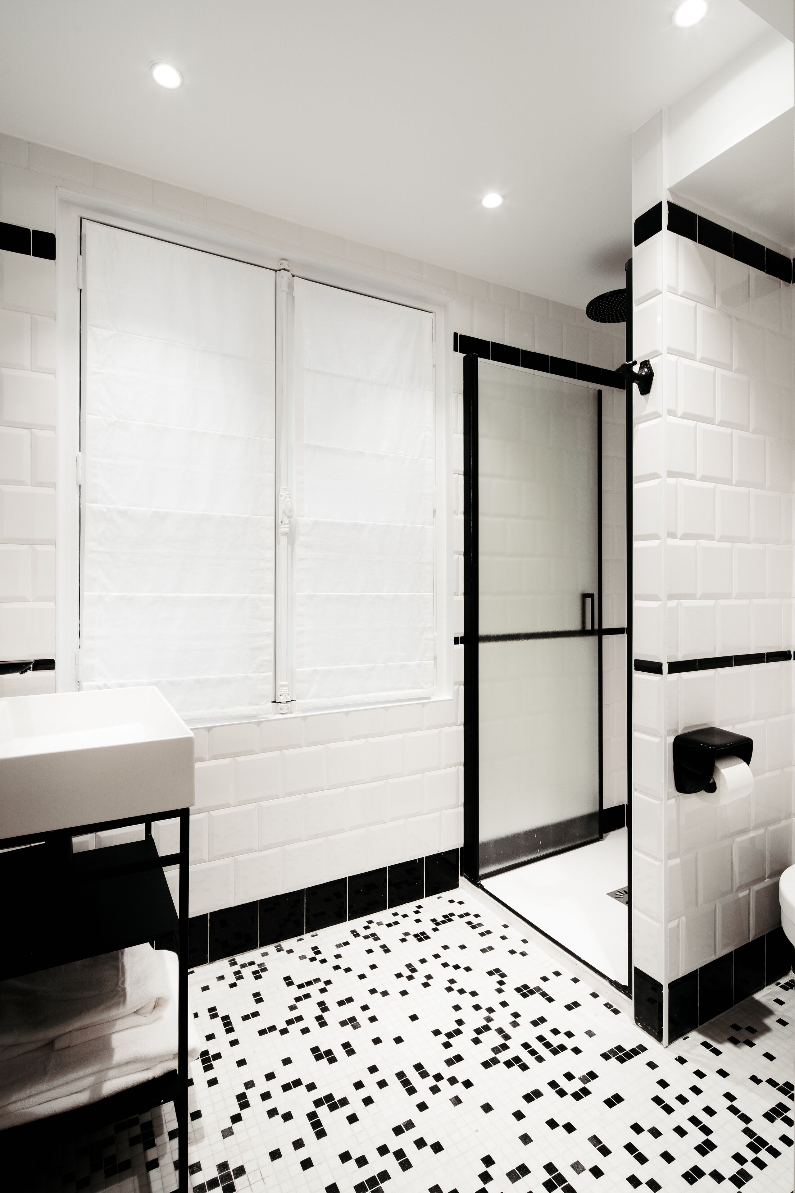 Une salle de bain moderne avec un sol carrelé en noir et blanc, une douche en verre et un lavabo blanc doté d’un plan de travail noir.