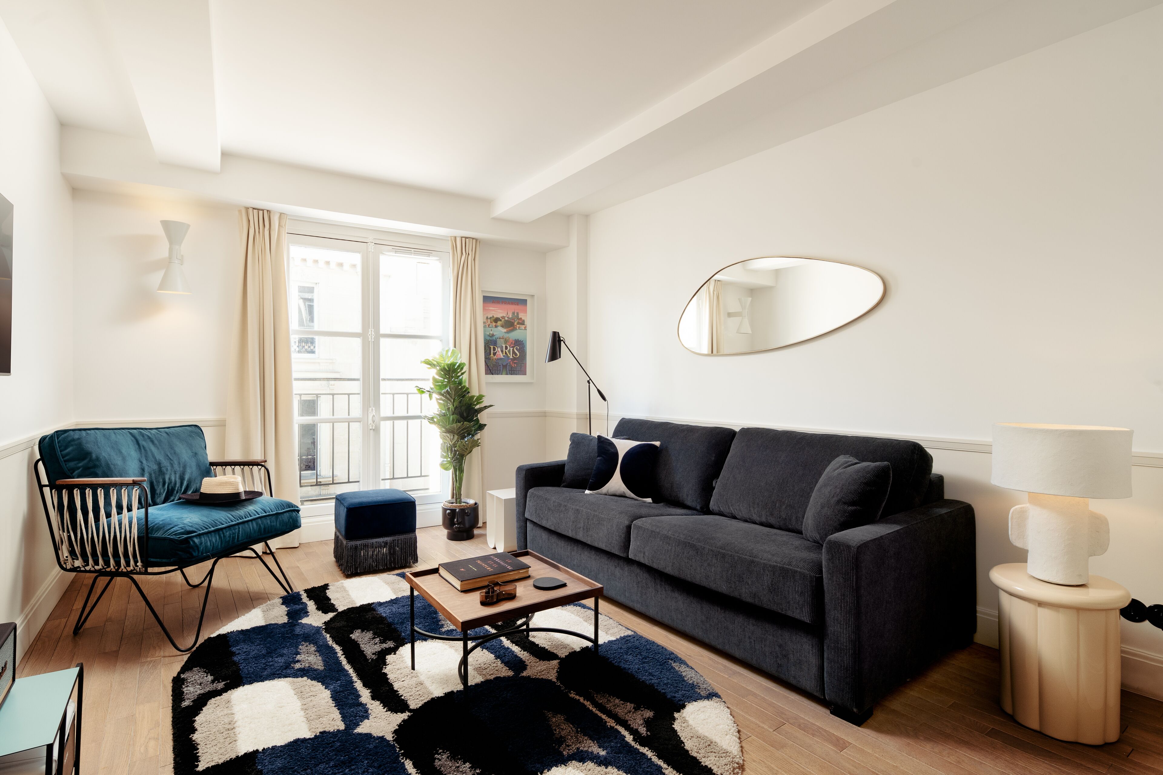 A modern living room with a dark grey sofa, a blue armchair, a wooden coffee table, and a large mirror on the wall.
