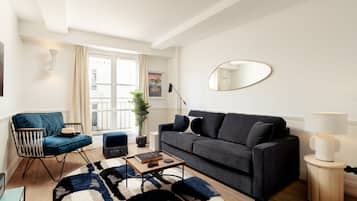 A modern living room with a dark grey sofa, a blue armchair, a wooden coffee table, and a large mirror on the wall.